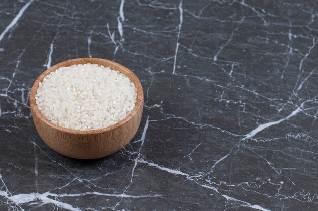 Wooden bowl full with raw rice on black.