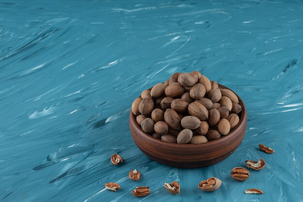 Wooden bowl of shelled organic walnuts on blue surface.