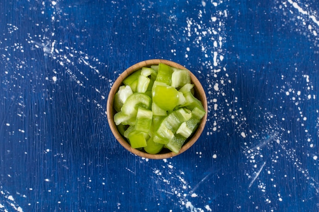 Free photo wooden bowl of sliced green bell peppers on marble surface