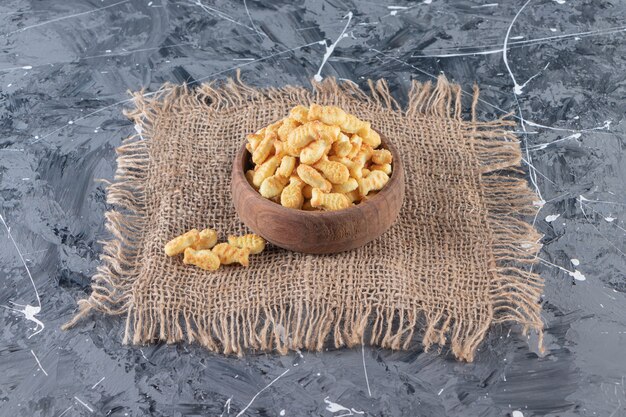 Wooden bowl of tasty salted crackers on marble surface.