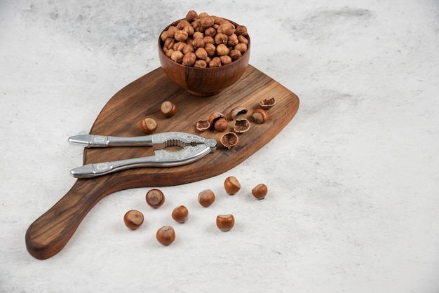 Wooden bowl of unpeeled organic hazelnut kernels on cutting board. 