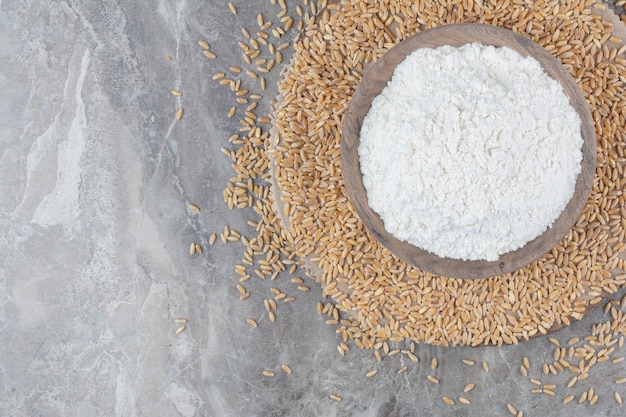 A wooden bowl with flour and oat grains on marble surface