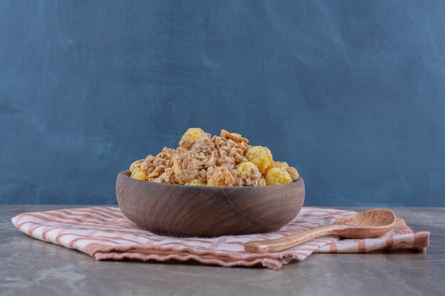 A wooden bowl with healthy cornflakes and an empty wooden spoon . 