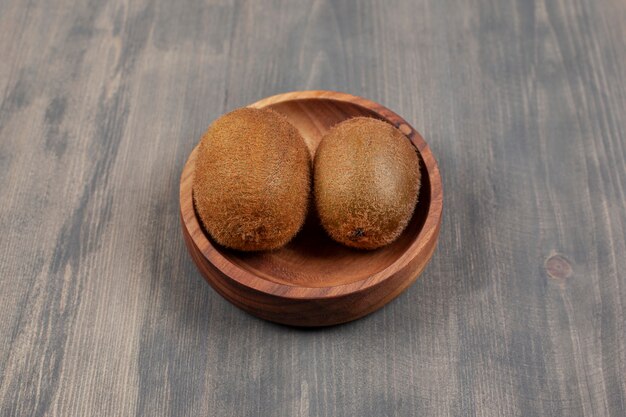 A wooden bowl with two fresh kiwis on a wooden table. High quality photo