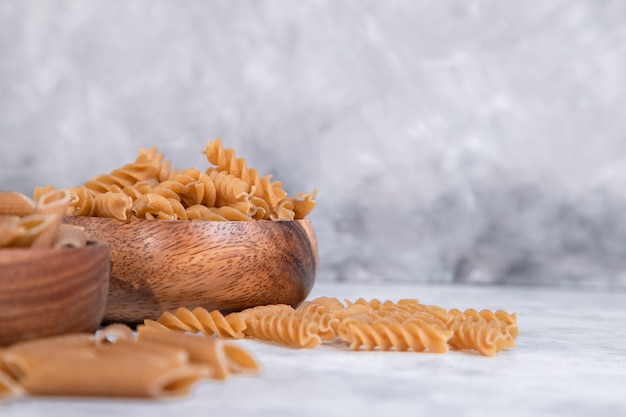 Wooden bowls of Italian uncooked dry pasta placed on stone table. High quality photo