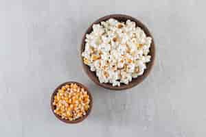 Free photo wooden bowls of popcorn and raw corn kernels on stone background.