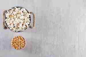 Free photo wooden bowls of popcorn and raw corn kernels on stone table.