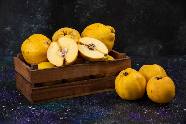 Wooden box of fresh ripe quinces on dark table. 