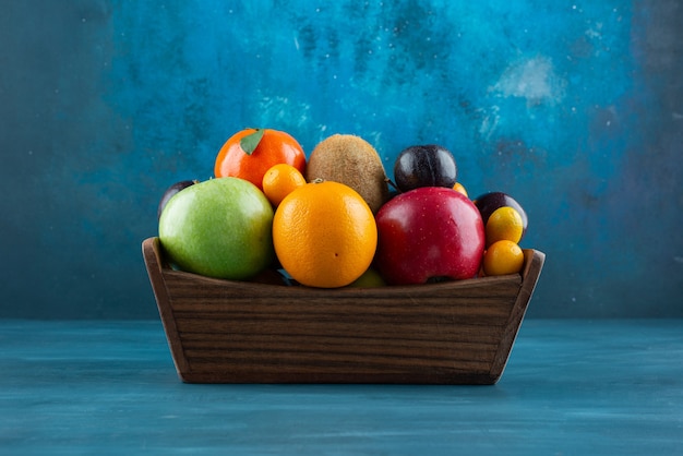 Free photo wooden box full of various organic fruits on blue surface.