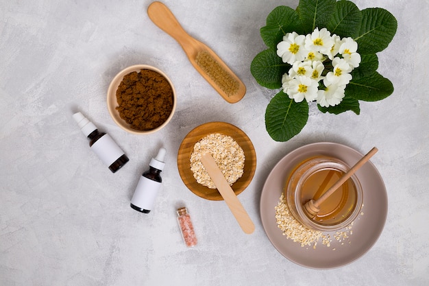 Free Photo wooden brush; honey; oats; himalayan rock salt; essential oil bottle with primula flowers vase on concrete background