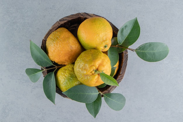 A wooden bucket filled with tangerines and leaves on marble . 