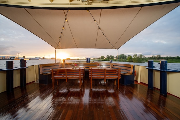 Wooden chairs and the tables with flowers and lanterns on top in the boat