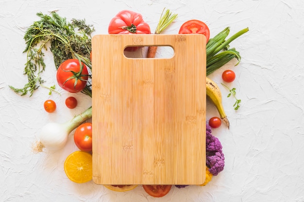 Wooden chopping board over the vegetables on texture backdrop