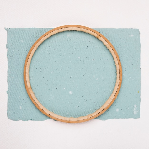 Free photo wooden circular border frame on blue paper against white backdrop