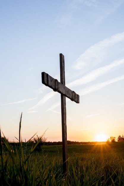 Free photo wooden cross in a grassy field with the sun shining in a blue sky