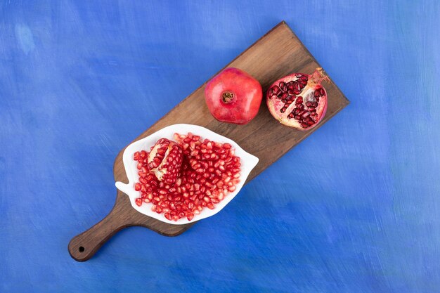 A wooden cutting board full of pomegranate on blue surface