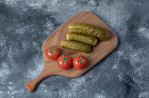 A wooden cutting board of tomatoes and pickled cucumber .