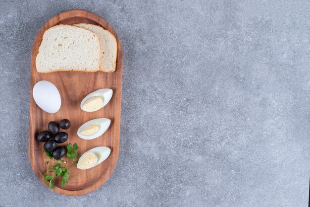 A wooden cutting board with boiled egg and slices of bread