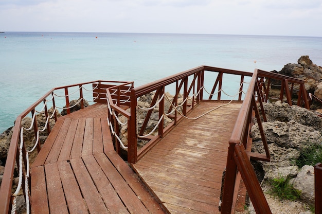 Free Photo wooden deck on the shore surrounded by rocks and sea under a cloudy sky