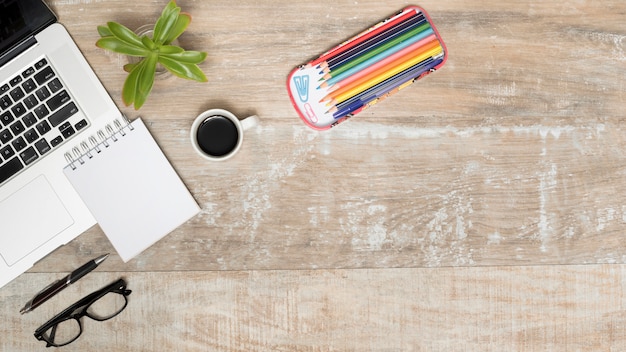 Wooden desk with opened laptop; tea; eye glasses; pen; plant and colorful pencils