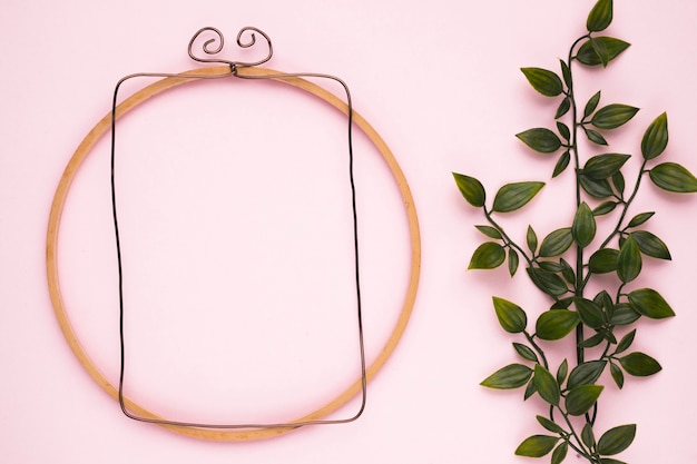 Free photo wooden frame near the artificial green plant on pink backdrop