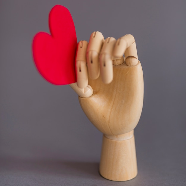 Free photo wooden hand holding red heart on table