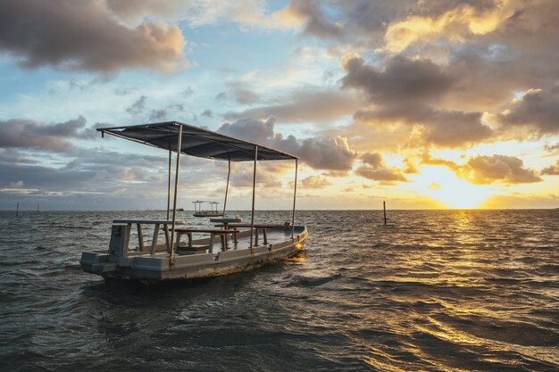 Wooden handmade boat on the sea under a cloudy sky and sunlight during the sunset