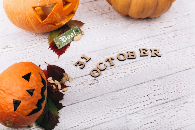 Wooden lettering '31 october' lies before large scarry Hallooween pumpkins on white table