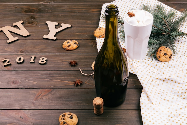 Wooden letters 'NY 2018' lie on the floor surrounded with cookies, fir branches, hot chocolate, empty bottle of wine