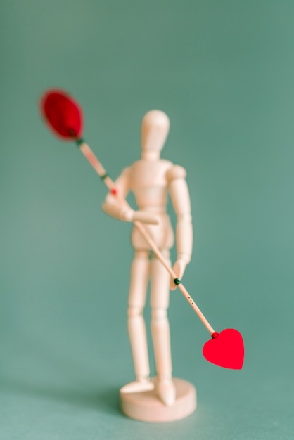 Wooden mannequin holding love arrow on green table