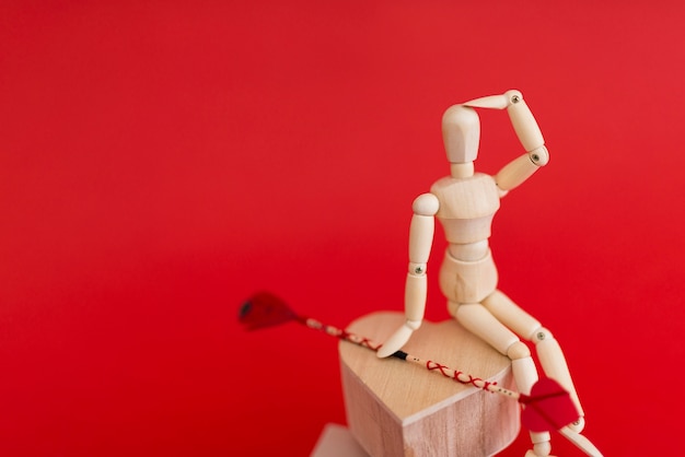 Free photo wooden mannequin sitting on heart with love arrow