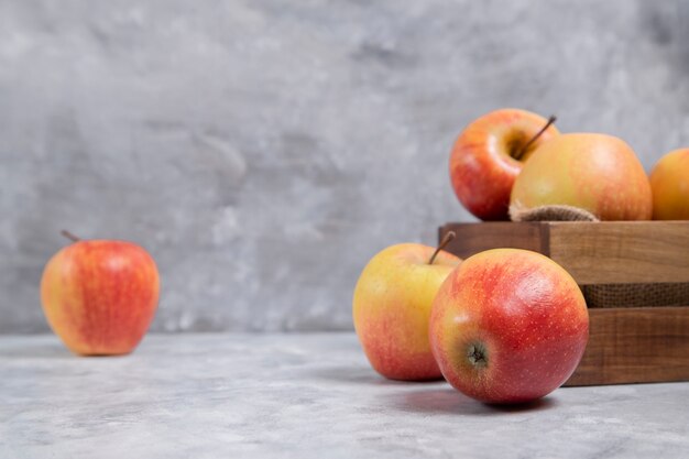 A wooden old box full of fresh ripe red apple fruits placed on a marble background . High quality photo