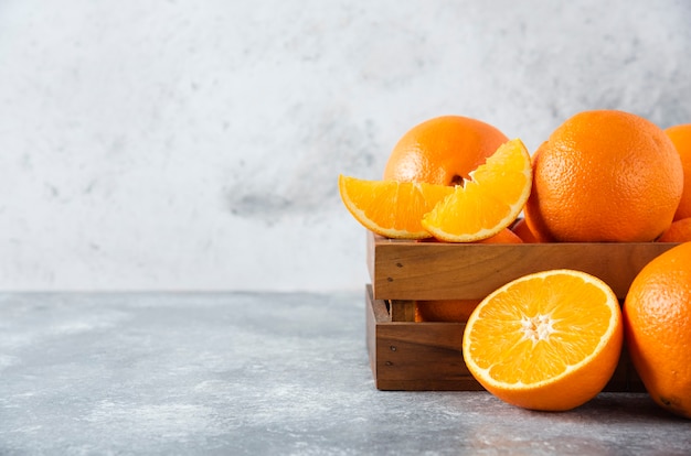 Free photo a wooden old box full of juicy orange fruit on stone table .