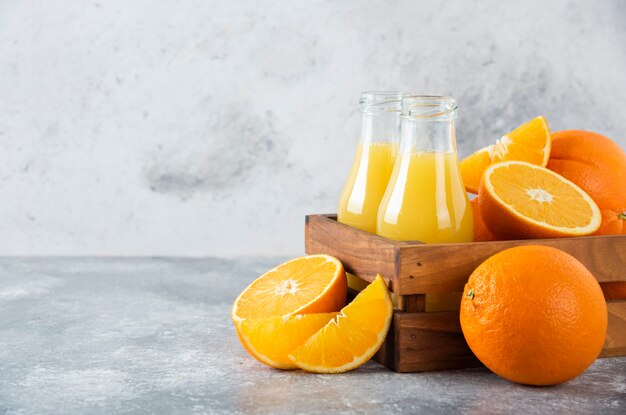 A wooden old box full of orange fruits and glass pitchers of juice on stone table .