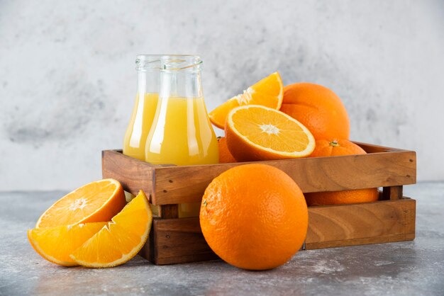 A wooden old box full of orange fruits and glass pitchers of juice on stone table .