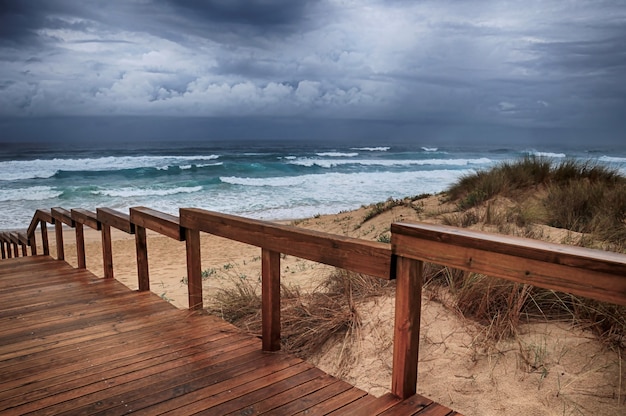 Free Photo wooden pathway on the beach by the breathtaking ocean waves under the cloudy sky