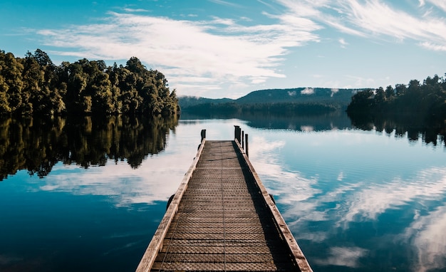 Free photo wooden pathway with trees and a blue sky reflected on lake mapourika waiho in new zealand