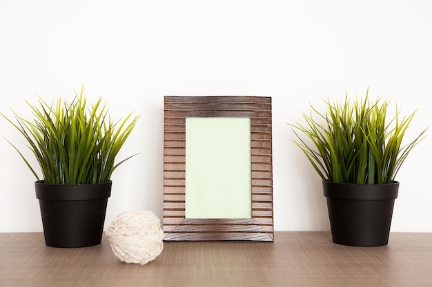 Free Photo wooden photo frame next to two pots with grass over a white background wall