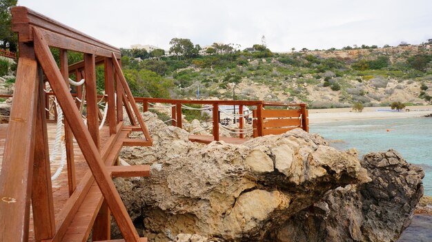 Wooden pier near the ocean surrounded by rocks under the blue sky