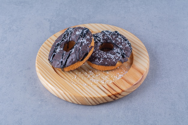 A wooden plate of delicious chocolate doughnuts with sprinkles . 