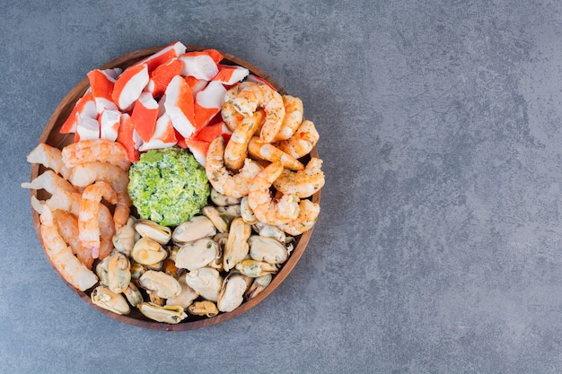 A wooden plate of delicious shrimps with tasty crab sticks on a stone surface 