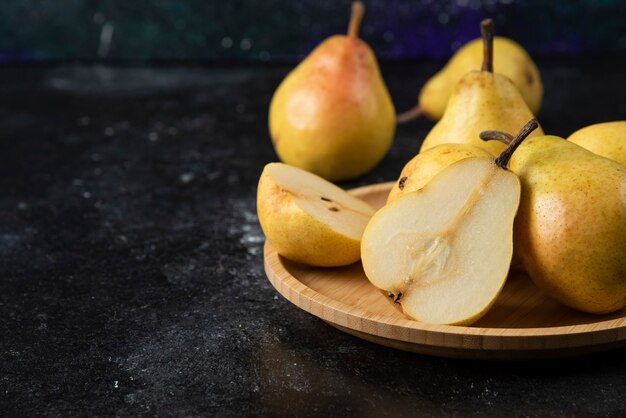 Wooden plate of delicious yellow pears on black surface. 