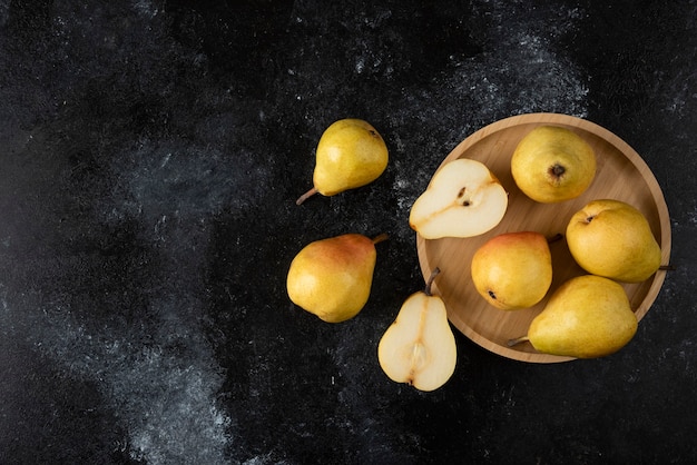 Free photo wooden plate of delicious yellow pears on black surface.