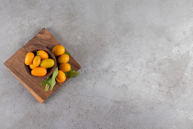 Wooden plate of fresh juicy kumquats on stone surface