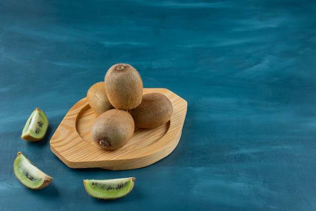 Wooden plate of fresh kiwi fruits on marble surface.