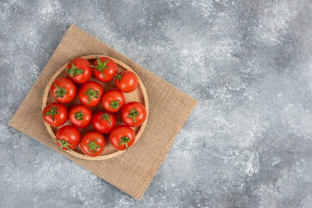 Wooden plate of fresh organic tomatoes on marble.