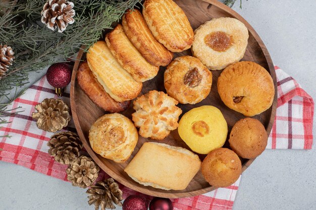 A wooden plate full of sweet pastries with Christmas balls and pinecones.