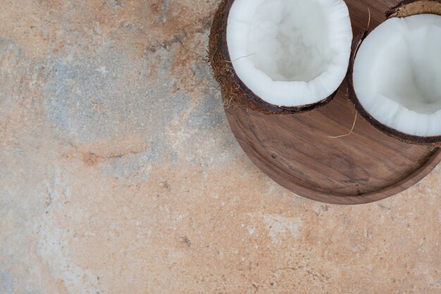 Free Photo wooden plate of half cut ripe coconuts on marble surface.