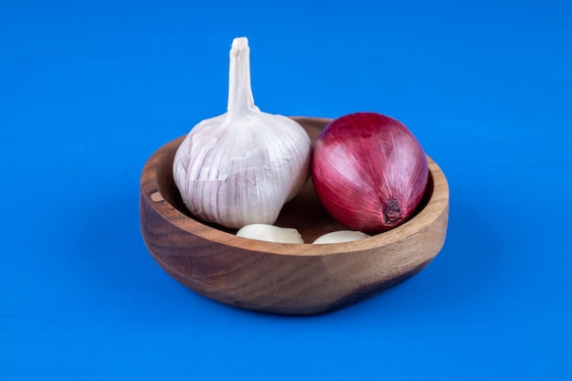 Wooden plate of purple onion and garlic on blue surface