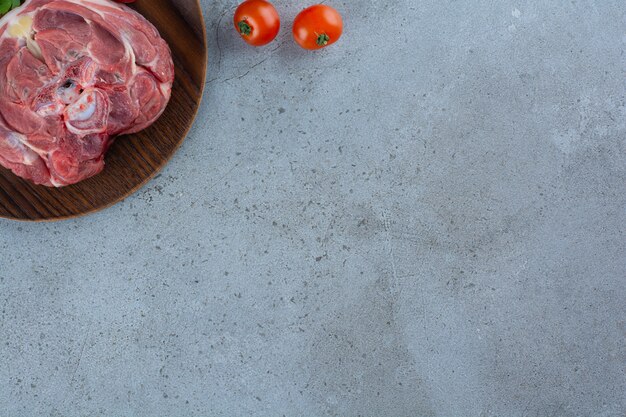 Wooden plate of raw beef steak on stone table.